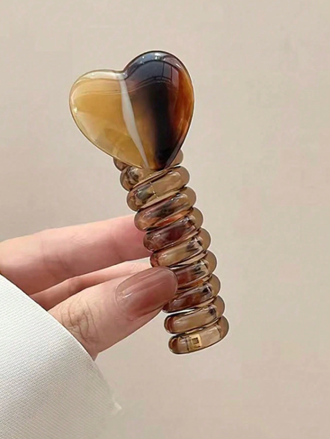 Heart-shaped stone with a textured handle held by a hand against a beige background