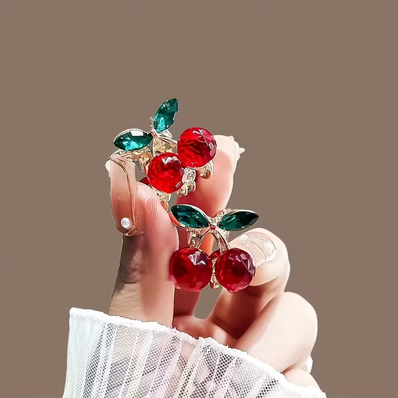 Decorative hair clips with red gemstones and green leaves held by a hand against a brown background