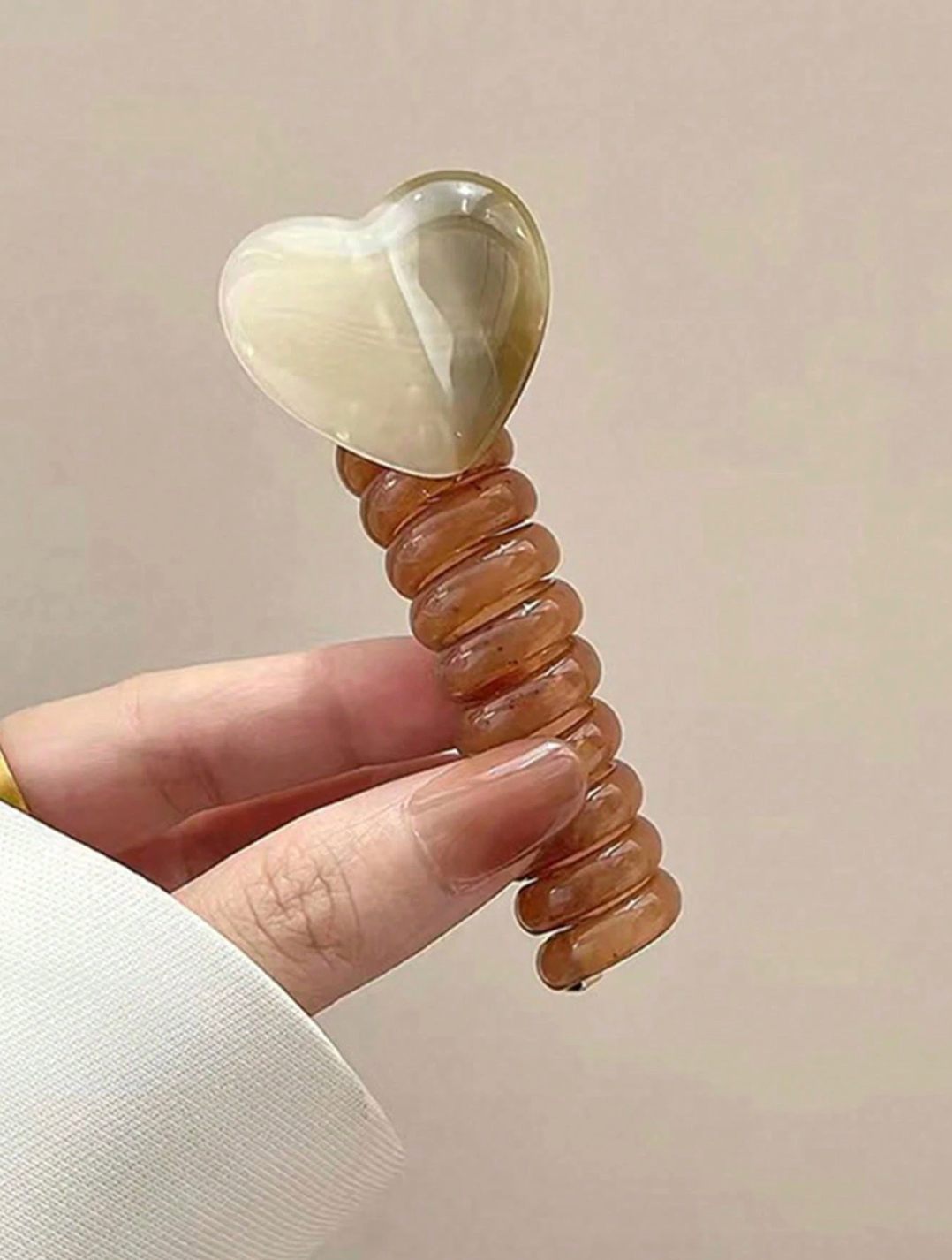 Heart-shaped object with ribbed design held by a hand against a plain background