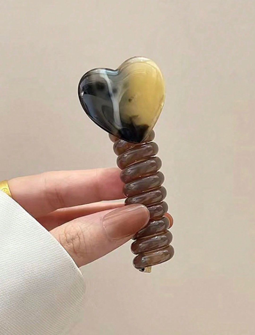 Heart-shaped hair accessory held by a hand against a beige background
