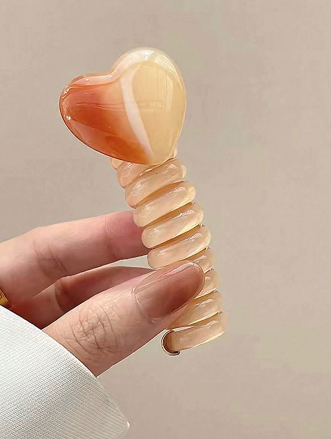 Heart-shaped object with ribbed design held by a hand against a neutral background