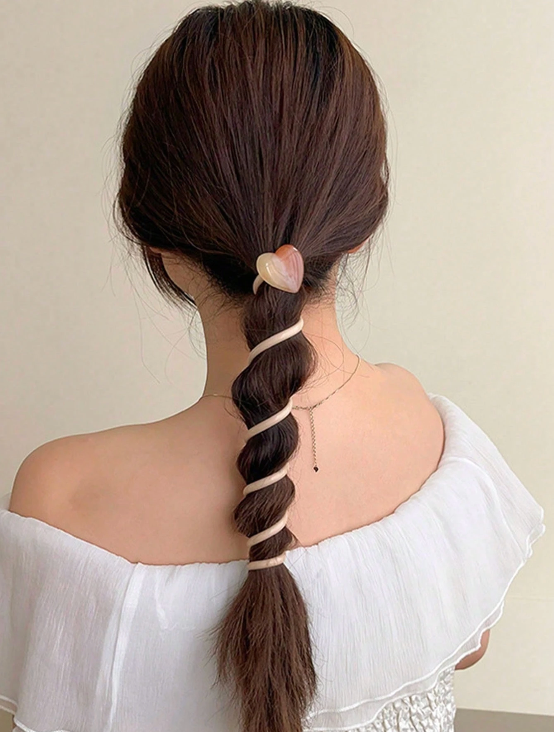 Person with braided hair wearing a white off-shoulder top on a plain background