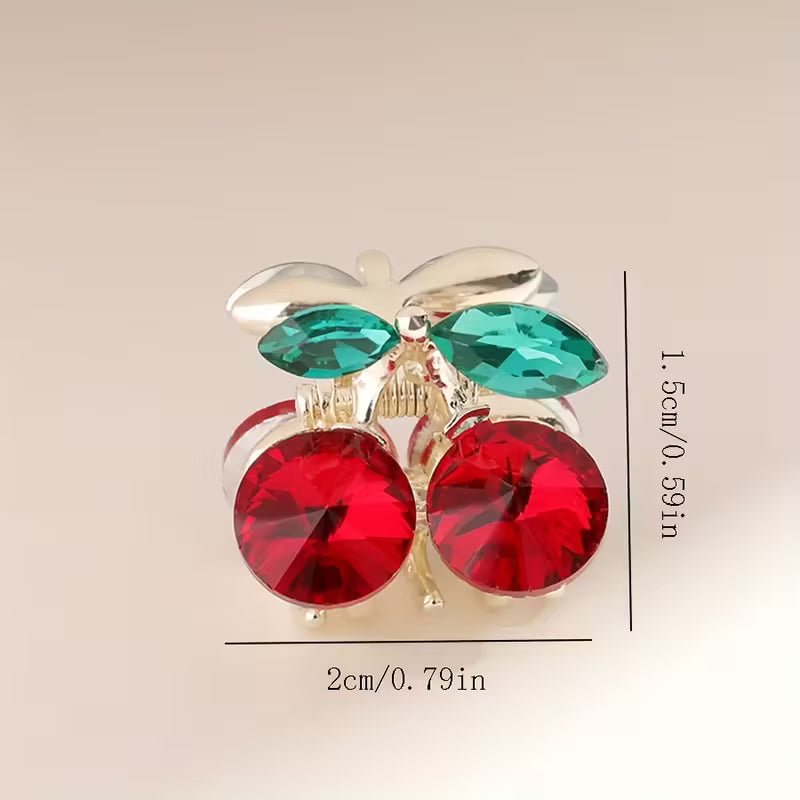 cherry-shaped hair clip with red and green gemstones on a beige background